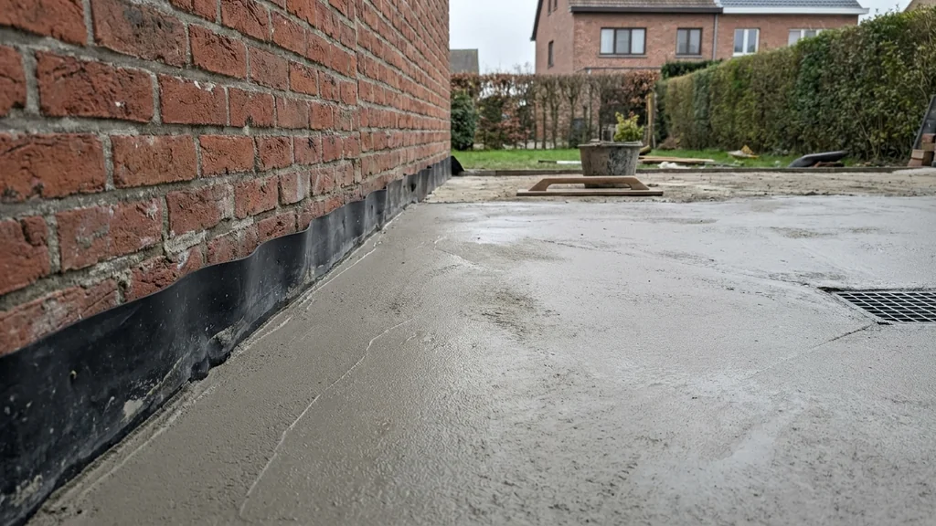Buitenchape voor een Vlaams achterterras met zichtbaar afschot richting afvoerputje, EPDM-waterdichting tegen de gevel; bakstenen achtergrond