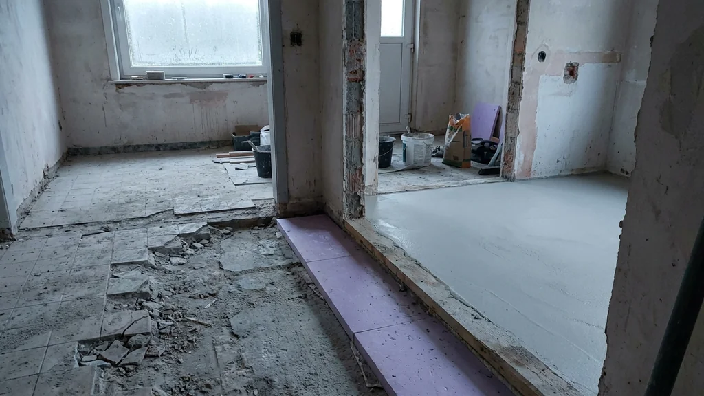 Renovatie-interieur met halve vloer opgebroken oude tegels en halve vloer met vers gelegde dunlaag-chape op PUR-isolatie — contrast tussen oud en nieuw werk